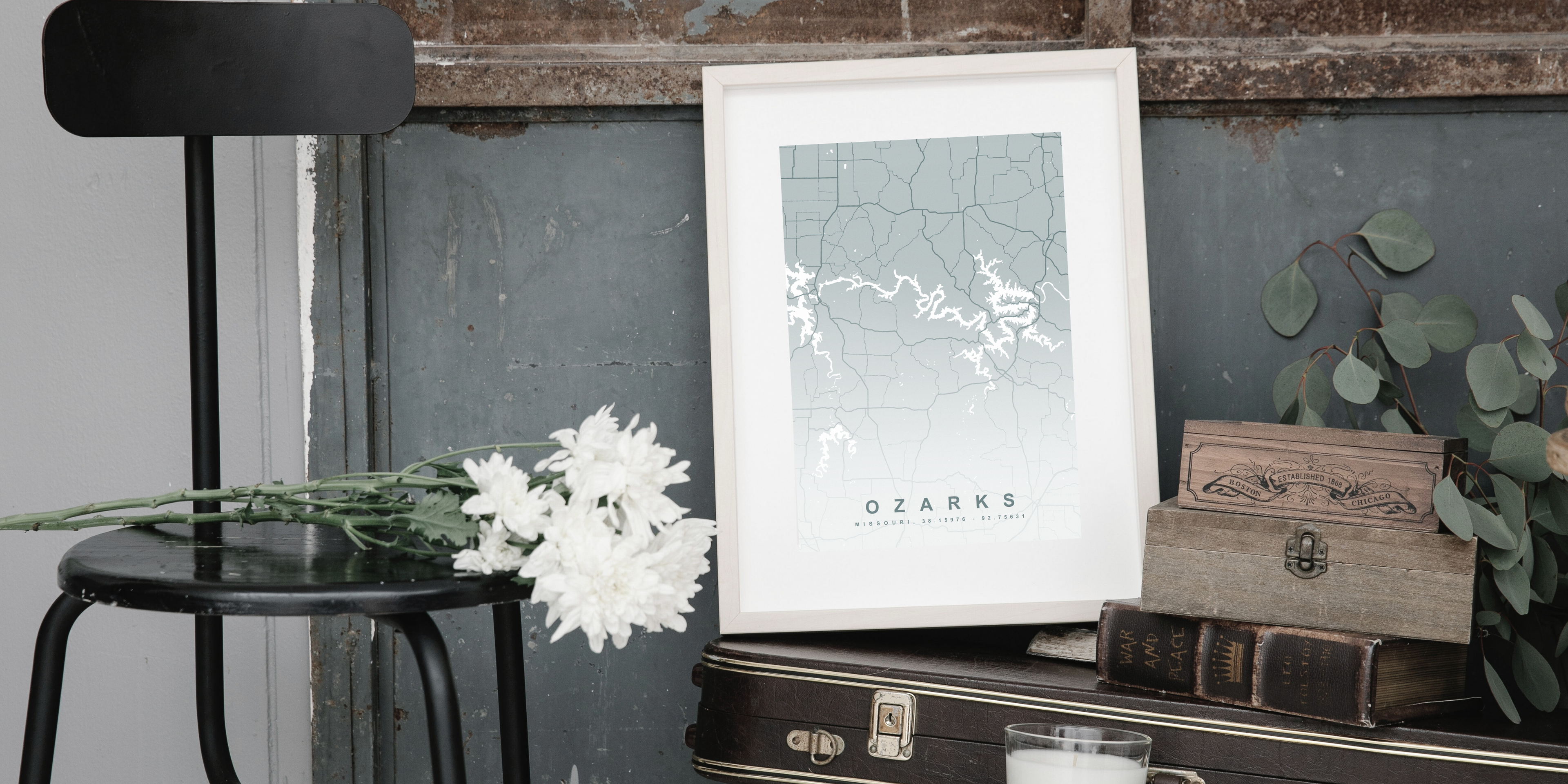 Framed map of the Ozarks on a table with a chair and plants.