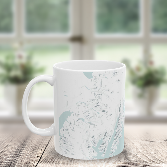 Atlas & Ink mug with blue and gray custom map design on a wooden surface with a blurred window background